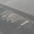 Vydřený asfalt od podvozků aut u odvodňovacího žlabu