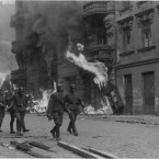 Příslušníci SS před hořící budovou. Německé jednotky během povstání vypalovali úkryty, stanoviště varšavských židů. Popelem lehly i synagogy